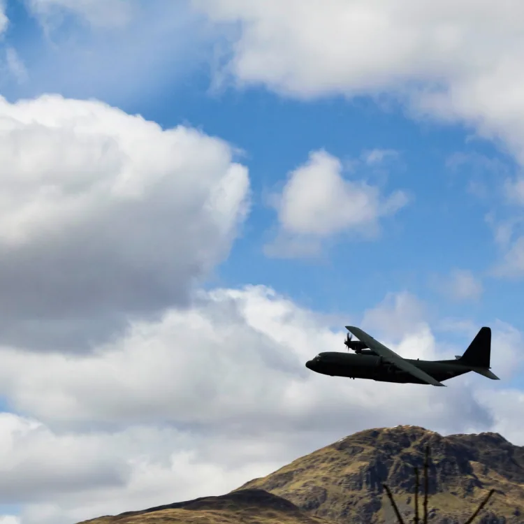 A C-130 transport aircraft climbing against a blue sky
